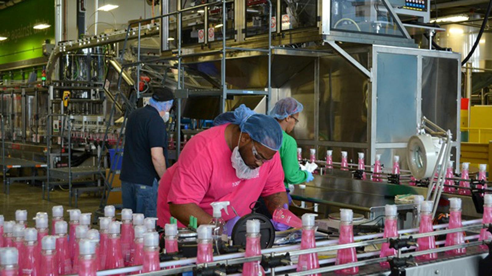 Women with hairnet at assembly line with pink bottles